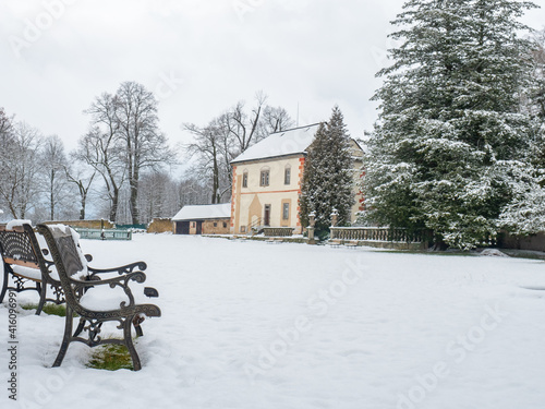 Winter alley park with a bench and historical building in snowy park photo