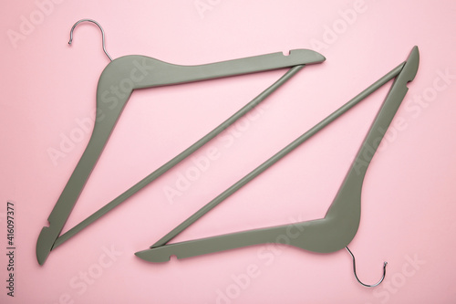 Two wooden grey hangers on pink background.