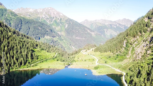 Alpine lake seen from above. The lake is surrounded with Alps overgrown with forest. The surface of the lake is calm, it reflects the mountains and sky. Clear and sunny day. Schladming region, Austria