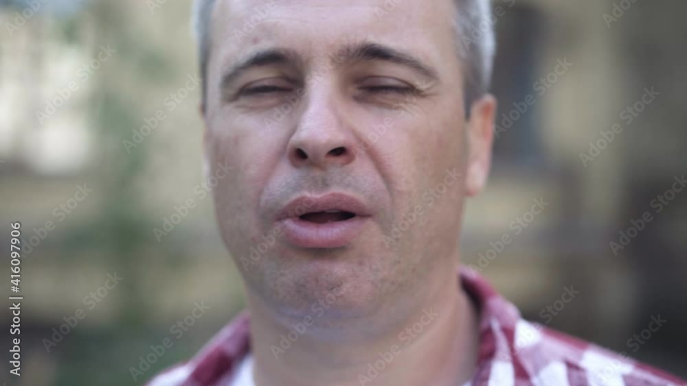 Headshot of confident Caucasian grey-haired man smoking outdoors blowing smoke looking at camera. Close-up portrait of addicted person having bad habit. Tobacco addiction. Headshot of confident Caucasian grey-haired man smoking outdoors blowing smoke looking at camera. Close-up portrait of addicted person having bad habit. Tobacco addiction.