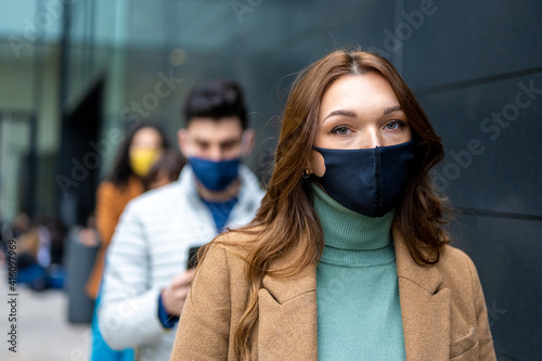beautiful eyes of a young redhead woman looking at the camera, tired and sad expression under facemask in quarantine time, crowd in queue waiting in line