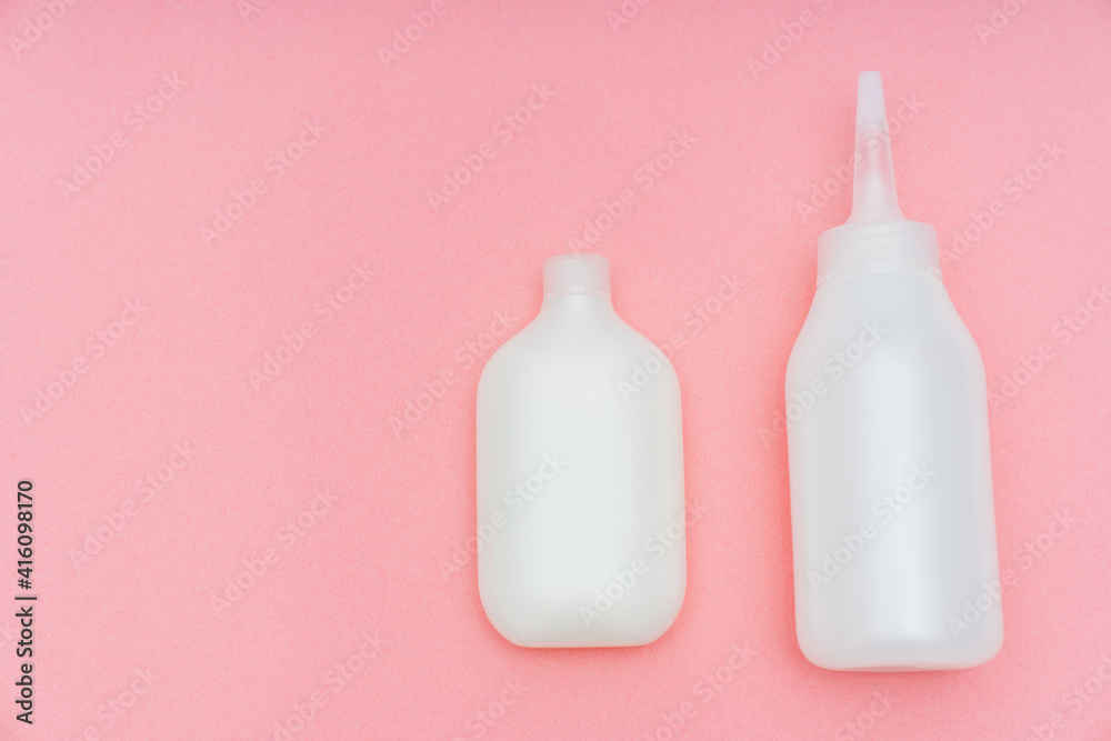 a white tube with paint and a bottle with a convenient applicator for the developing emulsion for self-dyeing hair at home on a pink background. saving time and money. home beauty salon. a white tube with paint and a bottle with a convenient applicator for the developing emulsion for self-dyeing hair at home on a pink background. saving time and money. home beauty salon.