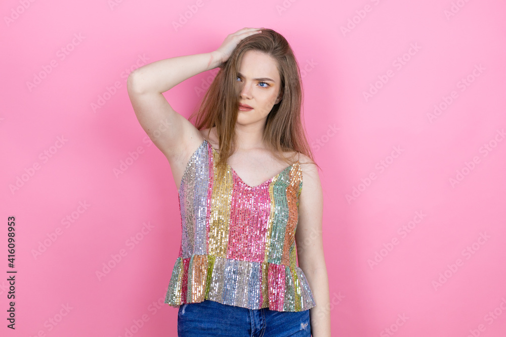 Pretty redhead woman wearing a shiny top standing over pink background putting one hand on her head smiling like she had forgotten something Pretty redhead woman wearing a shiny top standing over pink background putting one hand on her head smiling like she had forgotten something