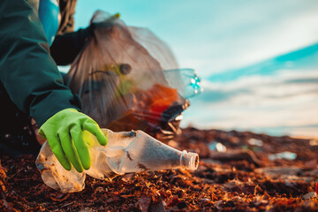 A worker in rubber gloes collects a plastic bottle on a beach. Hand close-up. The concept of Earth Day and ecology's problem