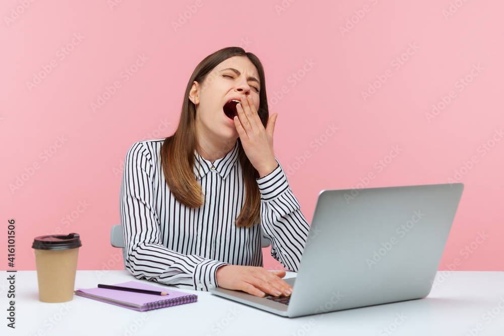 Tired overworked woman office worker yawning sitting at workplace with laptop, exhausted with job routine, showing disinterest. Indoor studio shot isolated on pink background Tired overworked woman office worker yawning sitting at workplace with laptop, exhausted with job routine, showing disinterest. Indoor studio shot isolated on pink background