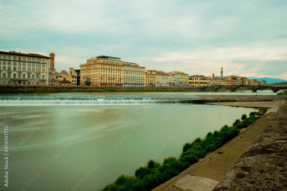 Fototapeta premium Long exposure river looking at colorful bright buildings day trip in Florence, Italy, Arno River