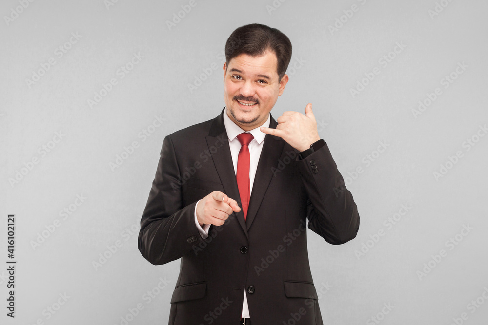 Call center. Businessman showing phone sign and smiling. indoor studio shot. isolated on gray background. handsome businessman with black suit, red tie and mustache looking at camera. Call center. Businessman showing phone sign and smiling. indoor studio shot. isolated on gray background. handsome businessman with black suit, red tie and mustache looking at camera.