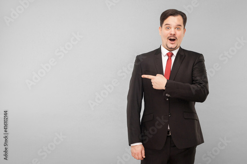 Amazement businessman pointing finger to copy space for your advertisement. Indoor, studio shot, isolated on gray background