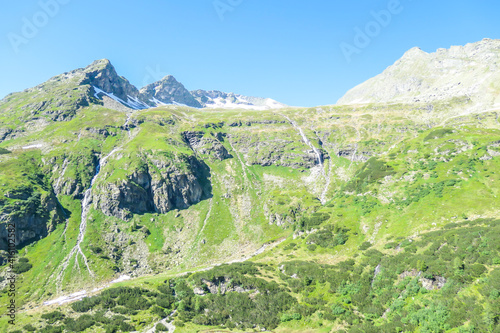 A panoramic view on Schladming Alps, partially still covered with snow. Spring slowly reaching the tallest parts of the mountains. Sharp peaks, slopes partially overgrown with lush green plants. photo