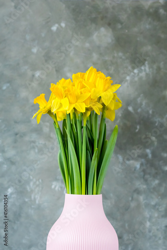 Spring flowers, yellow daffodils in a vase on a grey background. place for text. vertical photo. Easter concept. Copy space. 