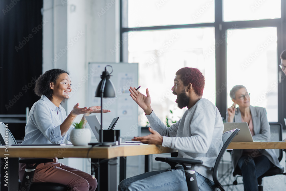 Obraz premium Smiling african american businesswoman pointing with hands near colleague