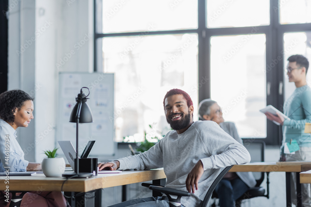 Smiling african american businessman sitting near laptop in office Smiling african american businessman sitting near laptop in office