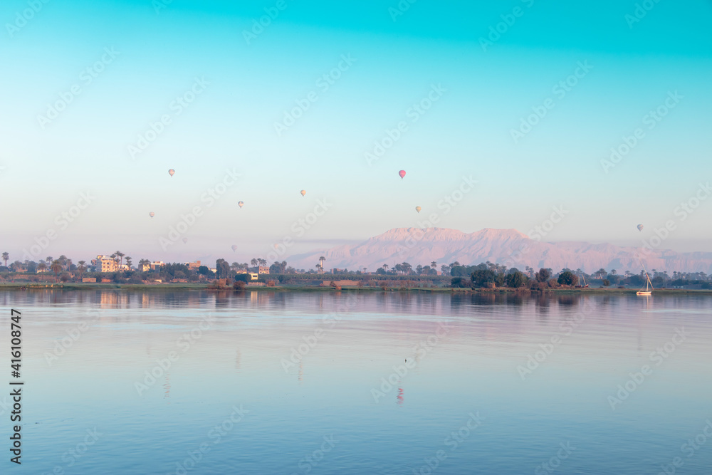 many hot air balloons floating over the Nile River in Luxor at sunrise 