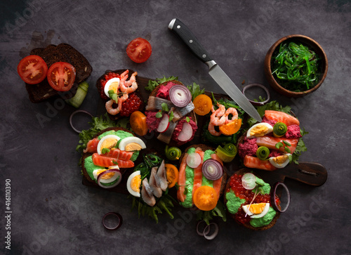 Smorrebrod, traditional Danish open sandwiches, dark rye bread with various fillings, black background, top view