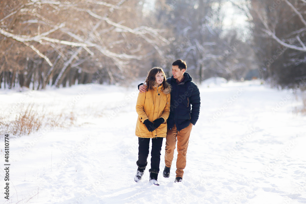 On a winter day, a young couple is walking in an embrace in the park and communicating