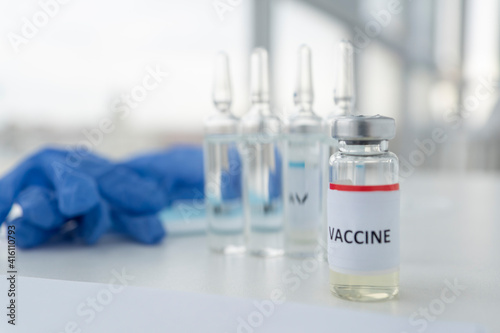 close up image of vial with inscription vaccine, other three ampoules and blue medical gloves not in focus. Healthcare and vaccination concept