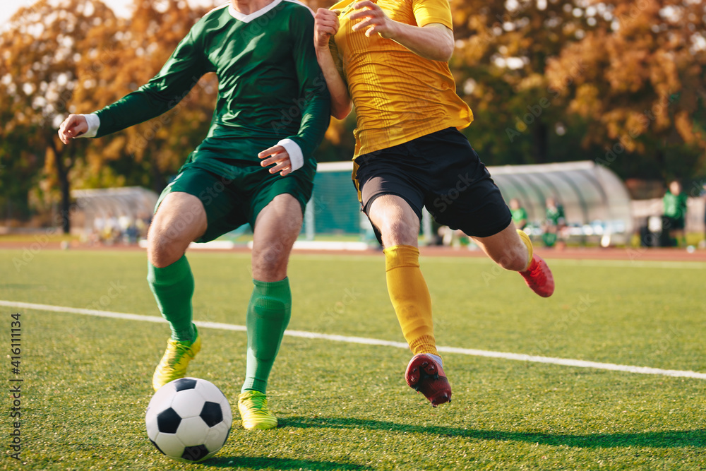 Two Footballers Running and Kicking Game. Adult Football Players Compete in Soccer Match. Soccer Bench and Substitute Players in the Blurred Background