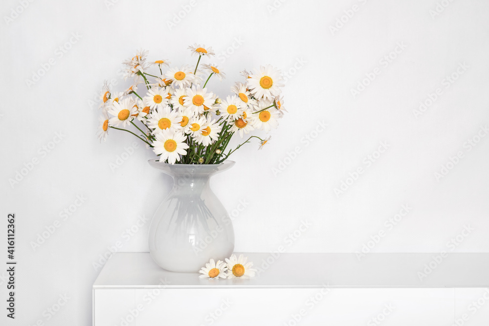 a bouquet of daisies in a white glass vase on a white table, flowers for grandmother's birthday, for women's day, flowers in a white interior