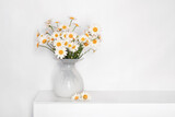 a bouquet of daisies in a white glass vase on a white table, flowers for grandmother's birthday, for women's day, flowers in a white interior