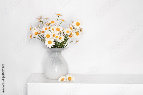 Fototapeta Naklejka Na Ścianę i Meble -  a bouquet of daisies in a white glass vase on a white table, flowers for grandmother's birthday, for women's day, flowers in a white interior