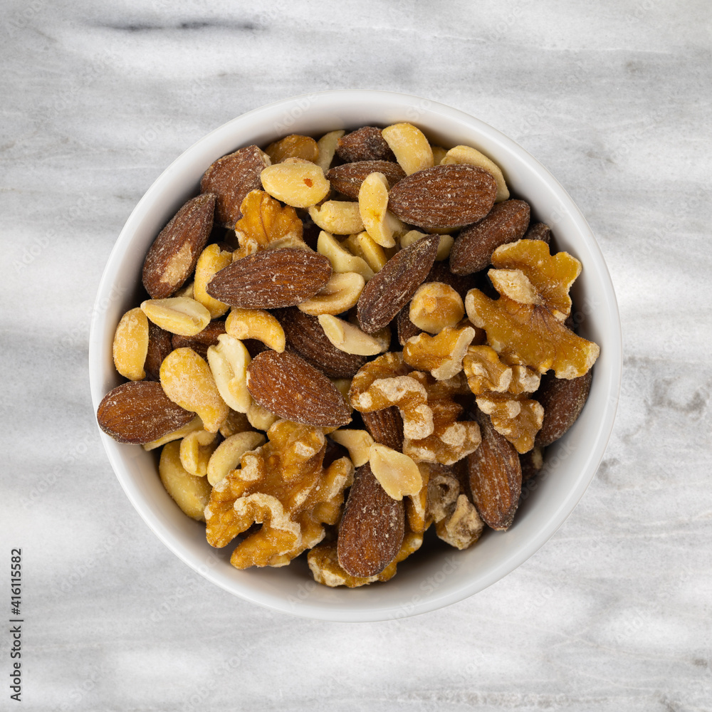 Top view of assorted nuts in a white bowl atop gray marble countertop. Top view of assorted nuts in a white bowl atop gray marble countertop.