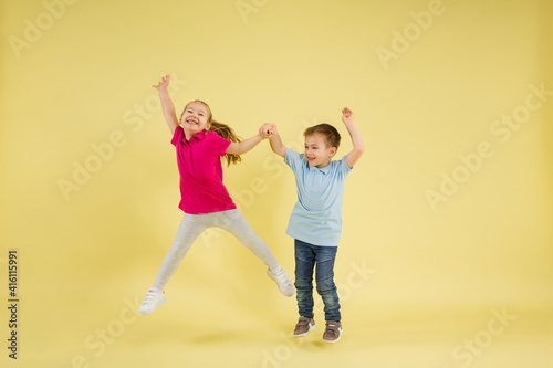 Jumping, dancing. Childhood and dream about big and famous future. Pretty little kids isolated on yellow studio background. Dreams, imagination, education, facial expression, emotions concept.
