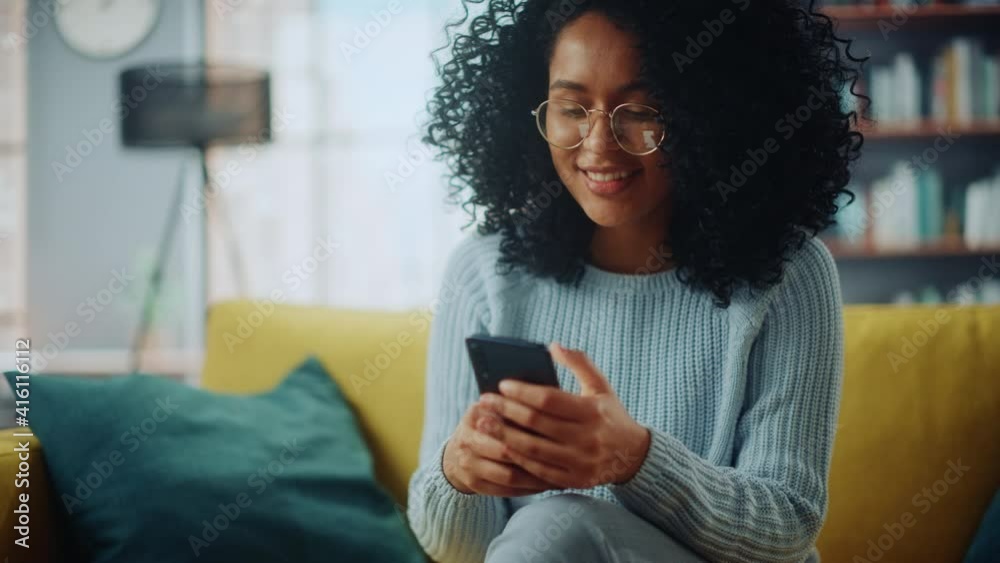 Portrait of a Beautiful Authentic Latina Female in a Stylish Cozy Living Room Using Smartphone at Home. She's Browsing the Internet and Checking Videos on Social Networks and Having Fun.