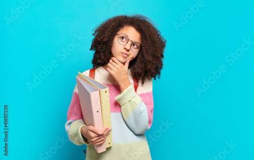 pretty afro teenager thinking, feeling doubtful and confused, with different options, wondering which decision to make. student concept photo