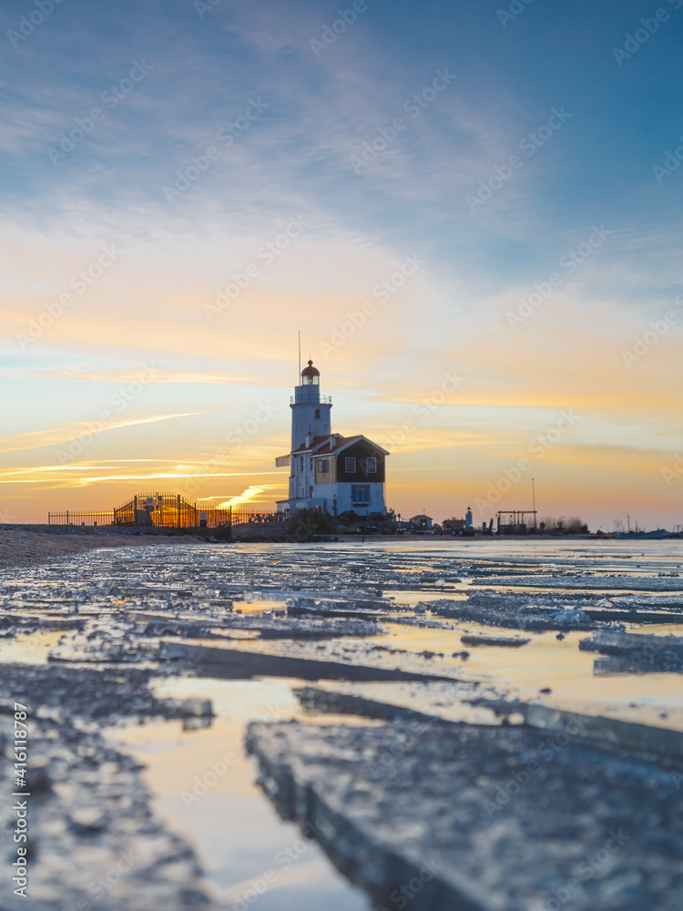 Winter landscape at the Lighthouse Paard van Marken Netherlands. On a cold day, temperature -7 degree during sunset. The IJsselmeer is frozen and by strong wind the shore was covered with ice
