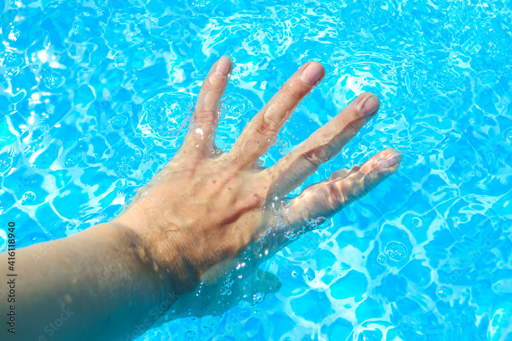 close-up - a woman's hand in the blue and clear water of the pool
