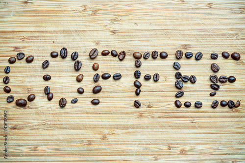 Ziarna kawy wysypane na drewniana deskę. Ziarna te tworzą napis COFFEE