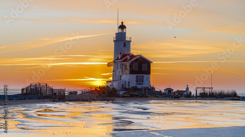 Winter landscape at the Lighthouse Paard van Marken Netherlands. On a cold day, temperature -7 degree during sunset. The IJsselmeer is frozen and by strong wind the shore was covered with ice photo