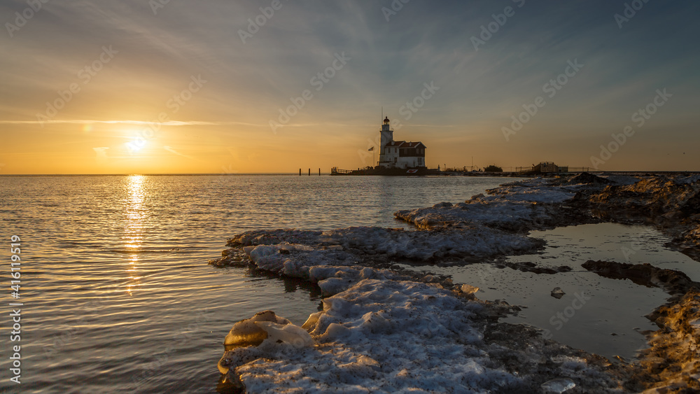 Winter landscape at the Lighthouse Paard van Marken Netherlands. On a cold day, temperature -7 degree during sunset. The IJsselmeer is frozen and by strong wind the shore was covered with ice