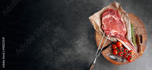 Obraz na płótnie fresh raw marbled beef steak with ingredients rosemary thyme cherry tomatoes pepper salt on a wooden table with a meat ax w salonie