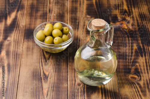 Olive oil in a bottle and fruits of olives in a bowl. Olive oil bottle and olives on wooden background with copy space.