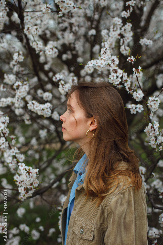 a girl stands sideways in a garden or park near a blooming apple tree apricot tree in spring a girl stands sideways in a garden or park near a blooming apple tree apricot tree in spring
