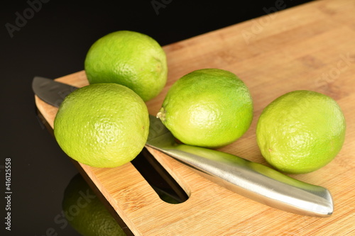 Several bright green juicy limes on a wooden dish, close-up, on a black background.