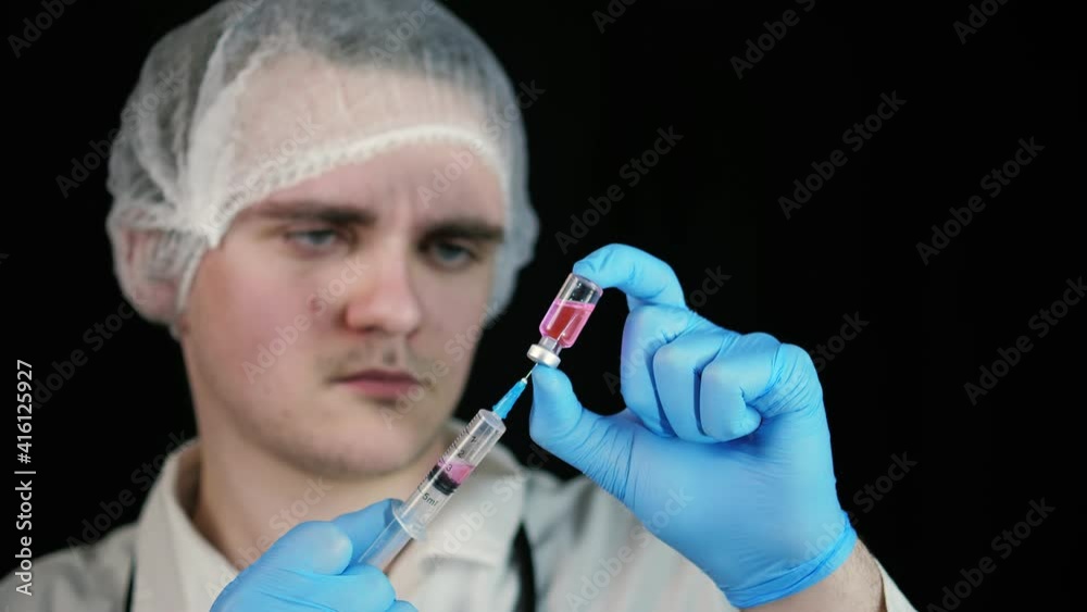 A young laboratory assistant draws pink liquid from an ampoule into a syringe. Focus on the syringe. isolated on black background. Doctor and scientist concept A young laboratory assistant draws pink liquid from an ampoule into a syringe. Focus on the syringe. isolated on black background. Doctor and scientist concept