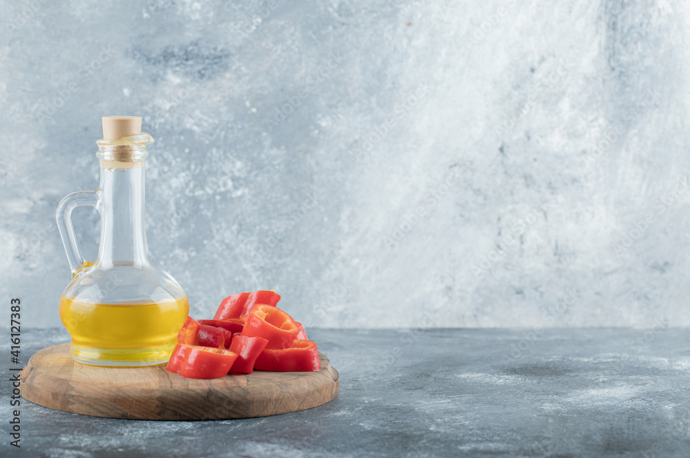 Obraz premium Sliced of sweet bell red pepper with a glass bottle of oil on a wooden board