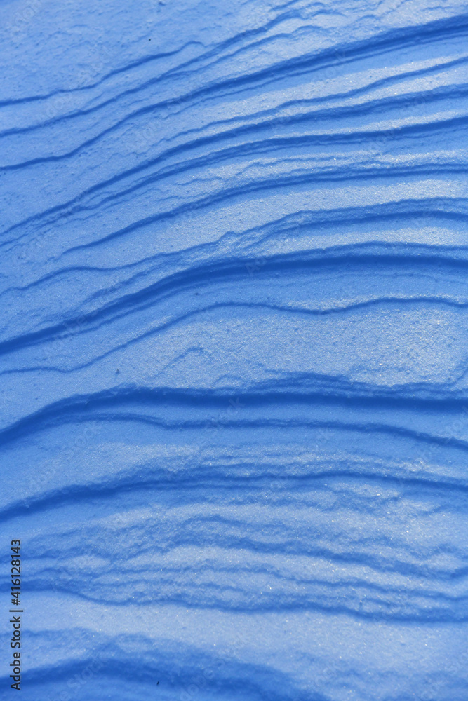 Obraz premium Wavy layers of glistening snow, illuminated by the winter sun in the evening. The surface of the ground is covered with snow. An imprint of a frozen blizzard in Scandinavia.