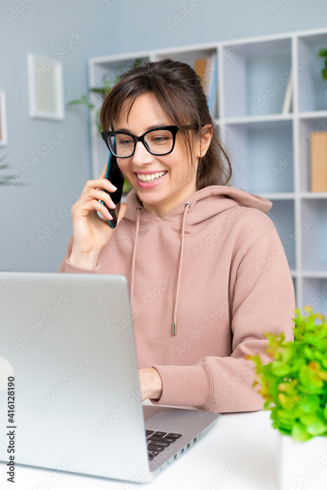 Portrait of a smiling beautiful young woman talking on the phone. Girl buys online store using laptop and smartphone. Portrait of a smiling beautiful young woman talking on the phone. Girl buys online store using laptop and smartphone.