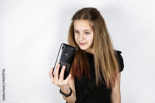 A young teen girl admires herself by looking at her phone like in a mirror, she tries to take a quality selfie photo to promote her account on social networks