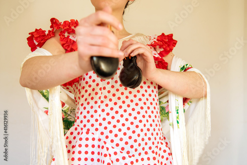 Detalle de una mujer española vestida con un vestido de lunares rojos de flamenca y un mantón de manila blanco tocando las castañuelas. Concepto de bailarina de sevillanas. Flamenco. photo