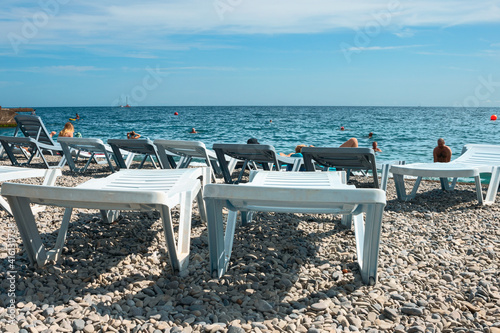 plastic sun loungers on a summer pebble beach against the backdrop of vacationing tourists and the blue sea