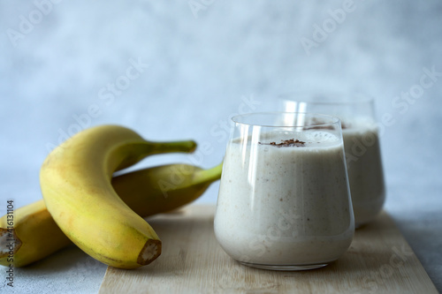 Two glasses with a milky banana cocktail on a bluish gray background. Next to the glasses are two bananas in the skin. Copy space. Selective focus.