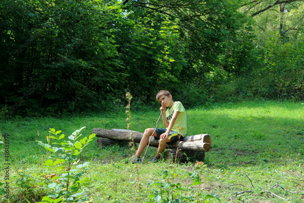 tired boy sitting on a wooden bench in a clearing in the forest tired boy sitting on a wooden bench in a clearing in the forest
