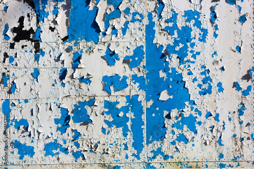 Grungy weathered metal surface with white old paint peeling off exposing old blue paint © Yann Wirthor