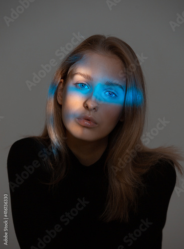 Portrait of young girl with blue neon light on face on gray studio background