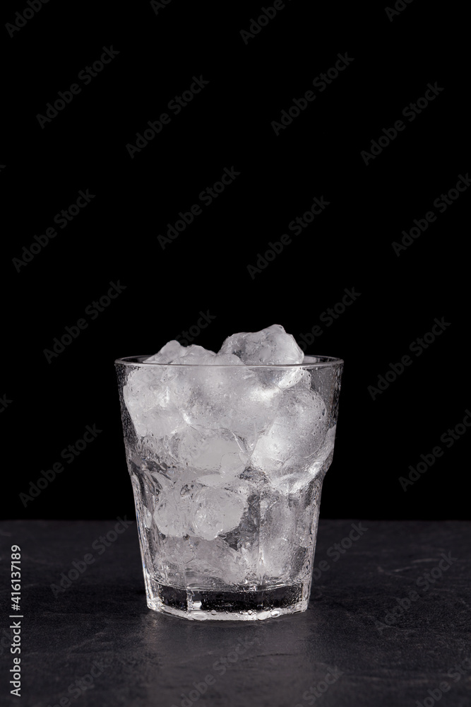 Close-up of glass clear glass filled with ice. Real ice cubes for making a drink or cocktail. Black background, vertical orientation, copy space