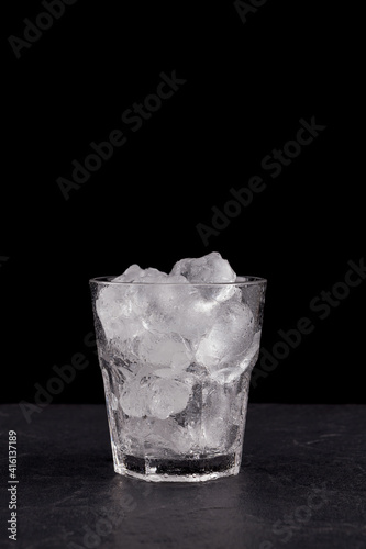 Close-up of glass clear glass filled with ice. Real ice cubes for making a drink or cocktail. Black background, vertical orientation, copy space